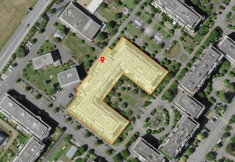 Aerial view of a building complex with multiple buildings, parking areas, and landscaped gardens.