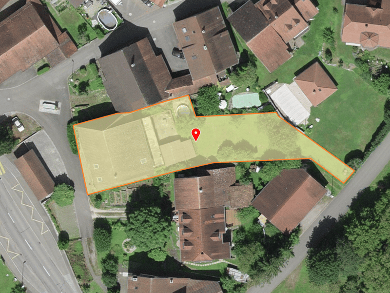 Aerial view of a residential area with several houses, a road, and a marked plot of land.