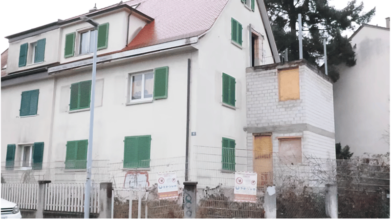 3 story house, white exterior, green shutters, red roof, fenced yard, some windows boarded up
