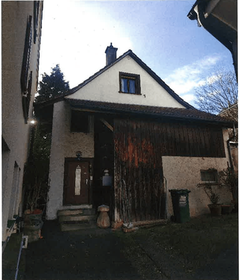2 story house, white walls, brown roof, wooden door, steps leading to the entrance, trash bin, plants