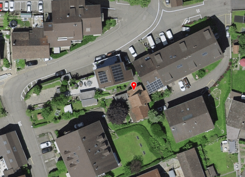 Aerial view of a residential area with multiple houses, solar panels on some roofs, and several cars parked in front of the houses.