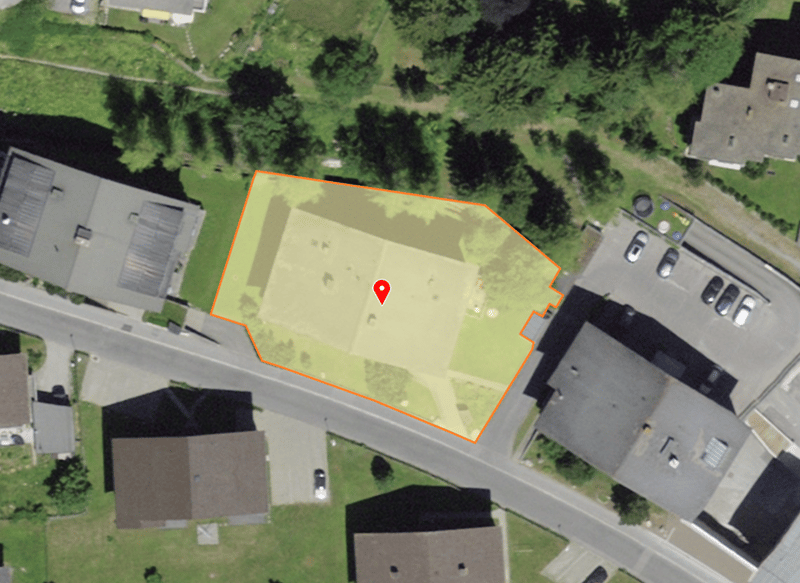 Aerial view of a property with a red pin indicating the location, surrounded by houses, trees, and a road.