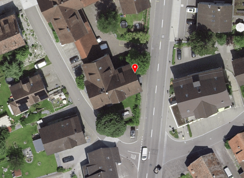 Aerial view of a neighborhood with several houses, some with solar panels, and cars parked in front of the houses.