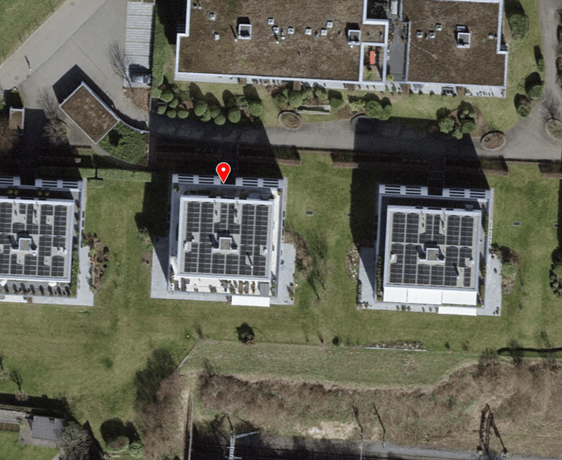 Three buildings with solar panels on the roof, surrounded by grass and bushes, located in a residential area