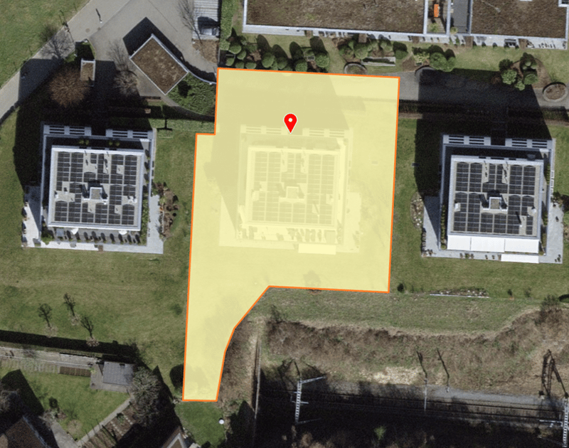 Plot of land with a building in the center, surrounded by two other buildings with solar panels on the roofs.