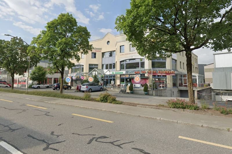 3-story building with restaurants on the ground floor. Trees and streetlight along the sidewalk. Cars parked on the side of the building.
