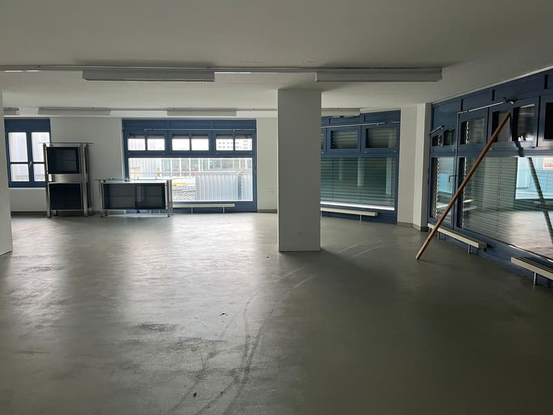 large open room, white walls, grey flooring, built-in cabinets, windows, bright natural light