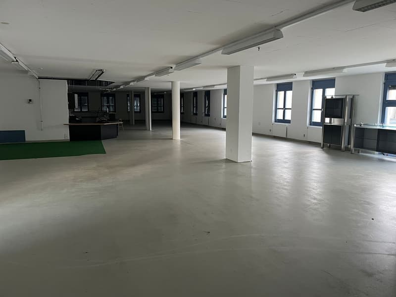 spacious room with large windows, metal pillars, ceiling lights, a desk, and green carpet