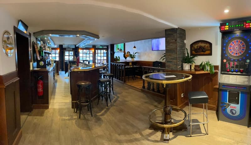 wooden flooring, wooden bar counter, chairs, dart board, stools, plant, fire extinguisher, mounted monitors, shelf with bottles, fire extinguisher