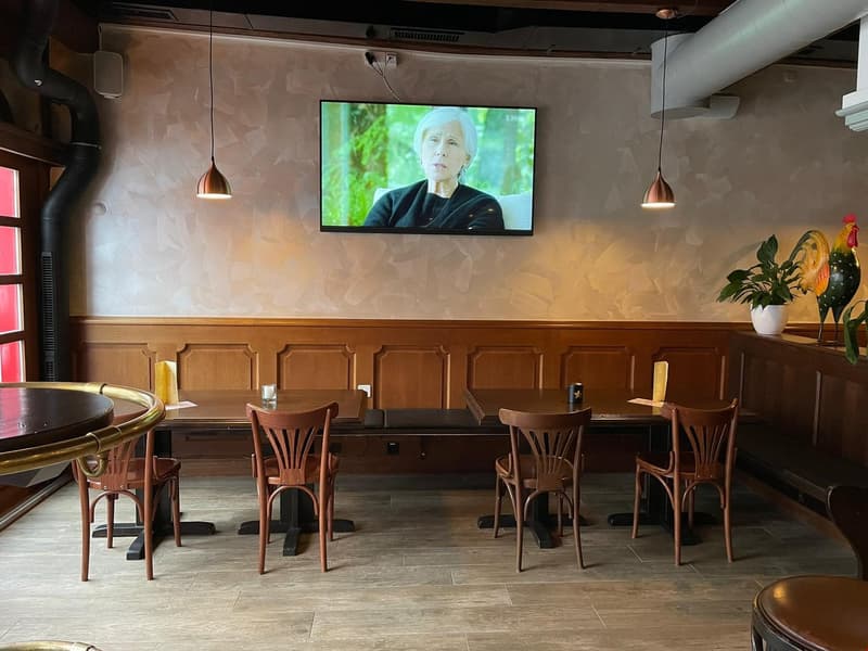 restaurant with wooden paneled walls, wooden tables and chairs, tiled floor, TV screen displaying a woman