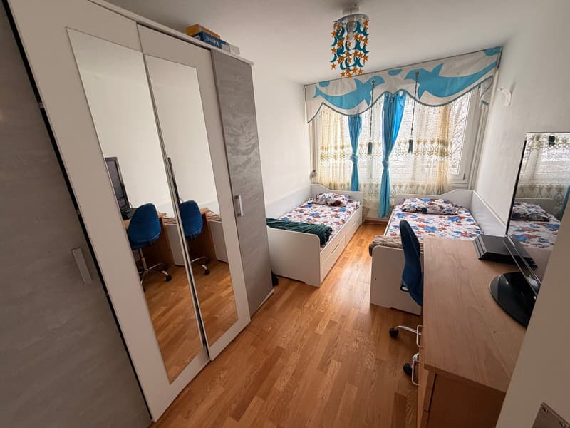 Room contains 2 single beds, desk with computer, chair, wardrobe with mirrors, window with curtains