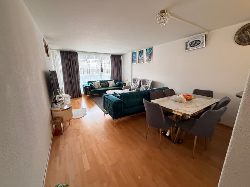 wood floor, window with curtains, chandelier, table with chairs, sofas, coffee table, TV, decorative objects, paintings on wall