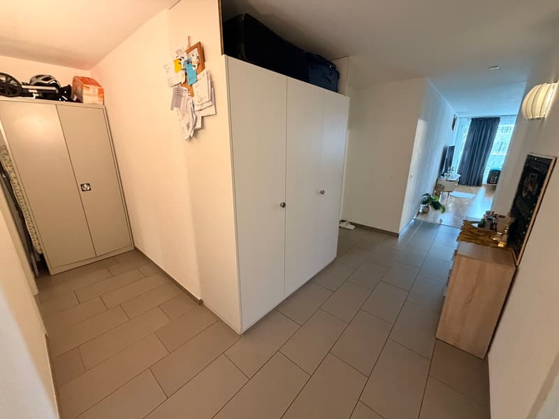 Empty hallway, tiled floor, white walls, large cabinets, small shelf with objects on top
