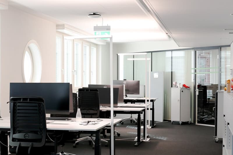 modern office with white walls, black chairs, white desks, computer monitors, glass windows, ceiling lights