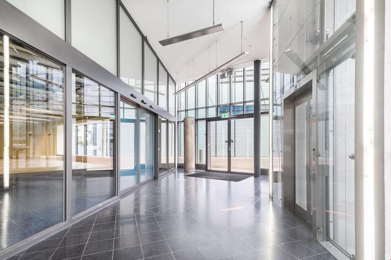 modern building with tiled flooring, large glass walls, elevators, and glass doors