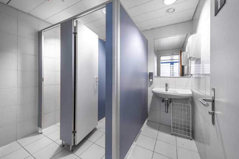 A bathroom with white tiles, a sink, a mirror, and two stalls with blue partitions.
