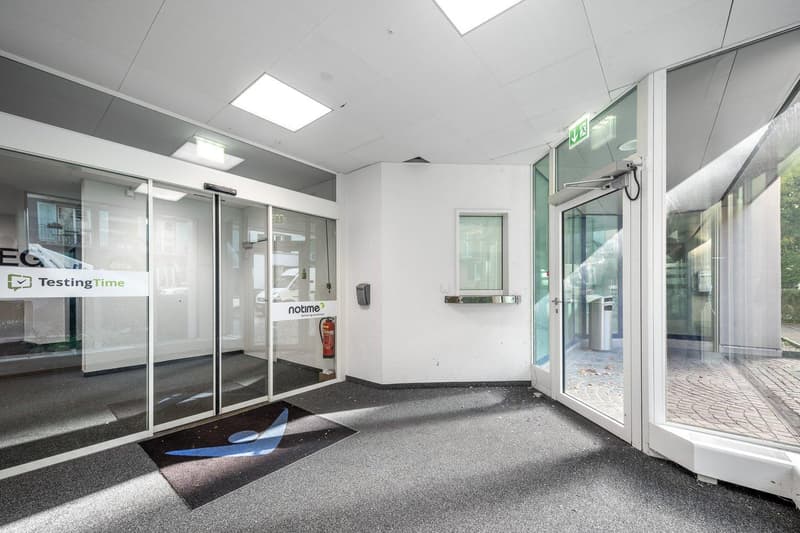 Empty room with glass walls, automatic sliding doors, carpet, fire extinguisher, and a sign that reads 'TestingTime'.