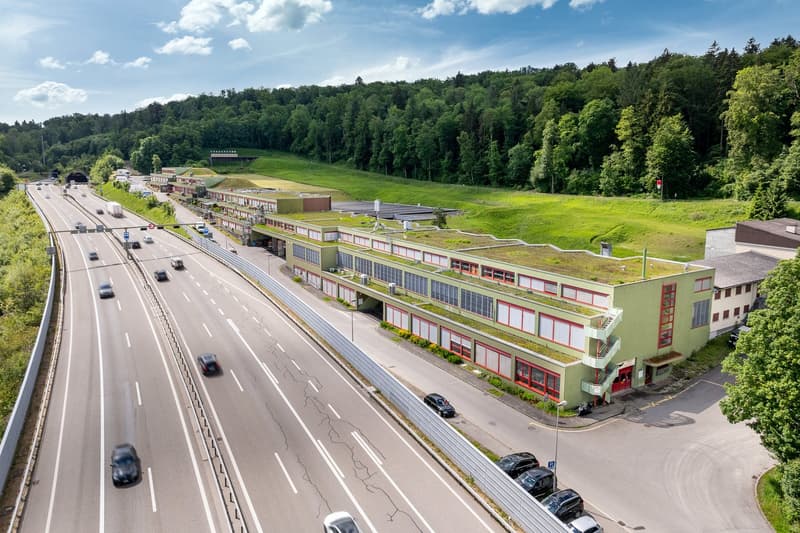 Industrial building complex near highway, greenery covering the roof, numerous large windows