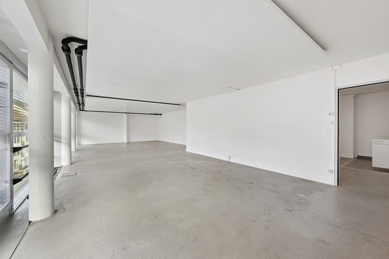 A large, empty room with white walls, concrete floor, and glass window on the left.