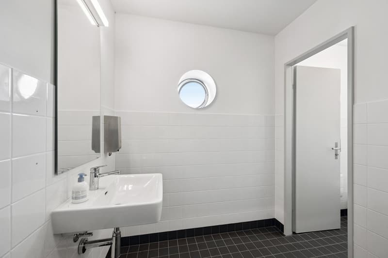 Modern, clean bathroom with white walls, tiled flooring, round window, white sink, and mirror.