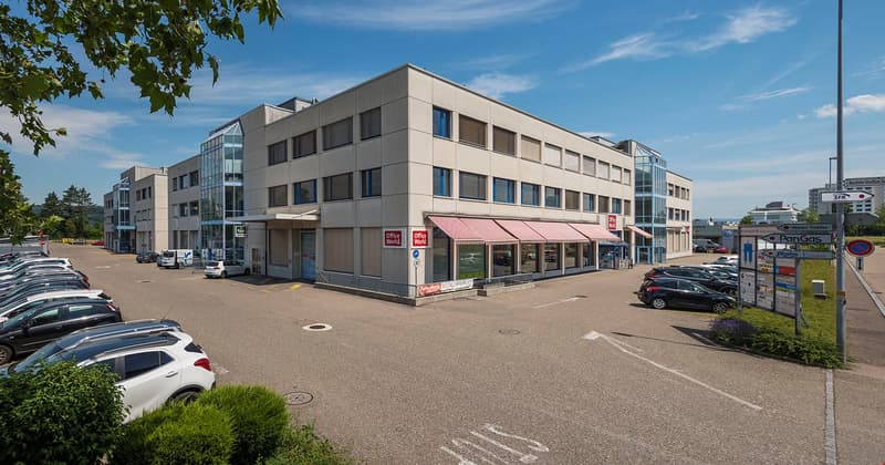 Modern office building, two-story, beige exterior, glass windows, red awnings, parking lot