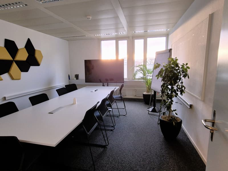 A conference room with a long table, black chairs, a whiteboard, a TV, and a potted plant.