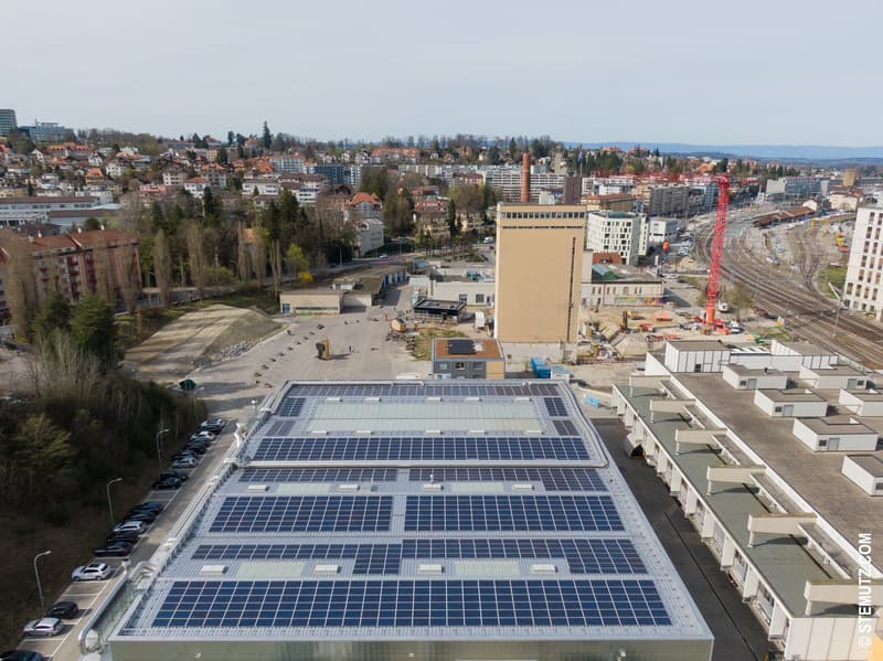 Industrial building with solar panels on the roof and cars parked outside