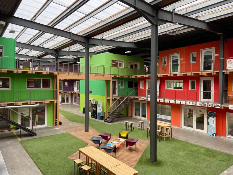 Multi-story modular building, green and red exteriors, open courtyard, seating area, wooden flooring, and multiple balconies