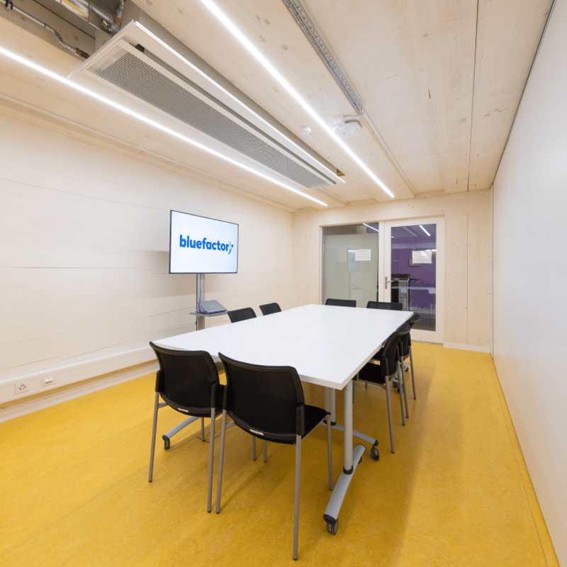 white walls, yellow floor, long white table, black chairs, monitor mounted on wall