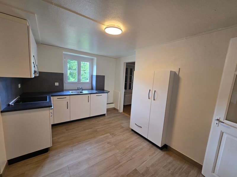 Newly renovated kitchen with white cabinets, black countertops, hardwood flooring, and a dishwasher. The kitchen has a sink and a window overlooking the outdoors.