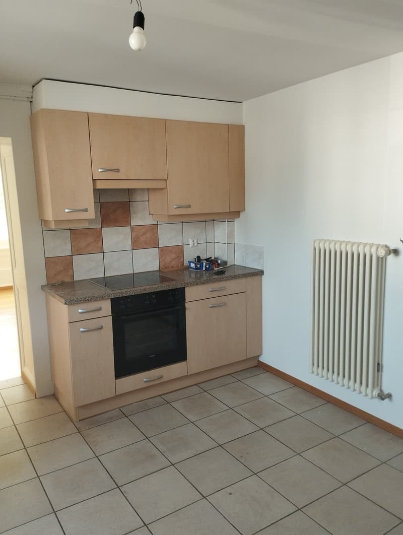 The image shows a kitchen with light-colored wood cabinets, a black oven, and tile flooring. The kitchen appears to have a dishwasher, which is one of the visible features.