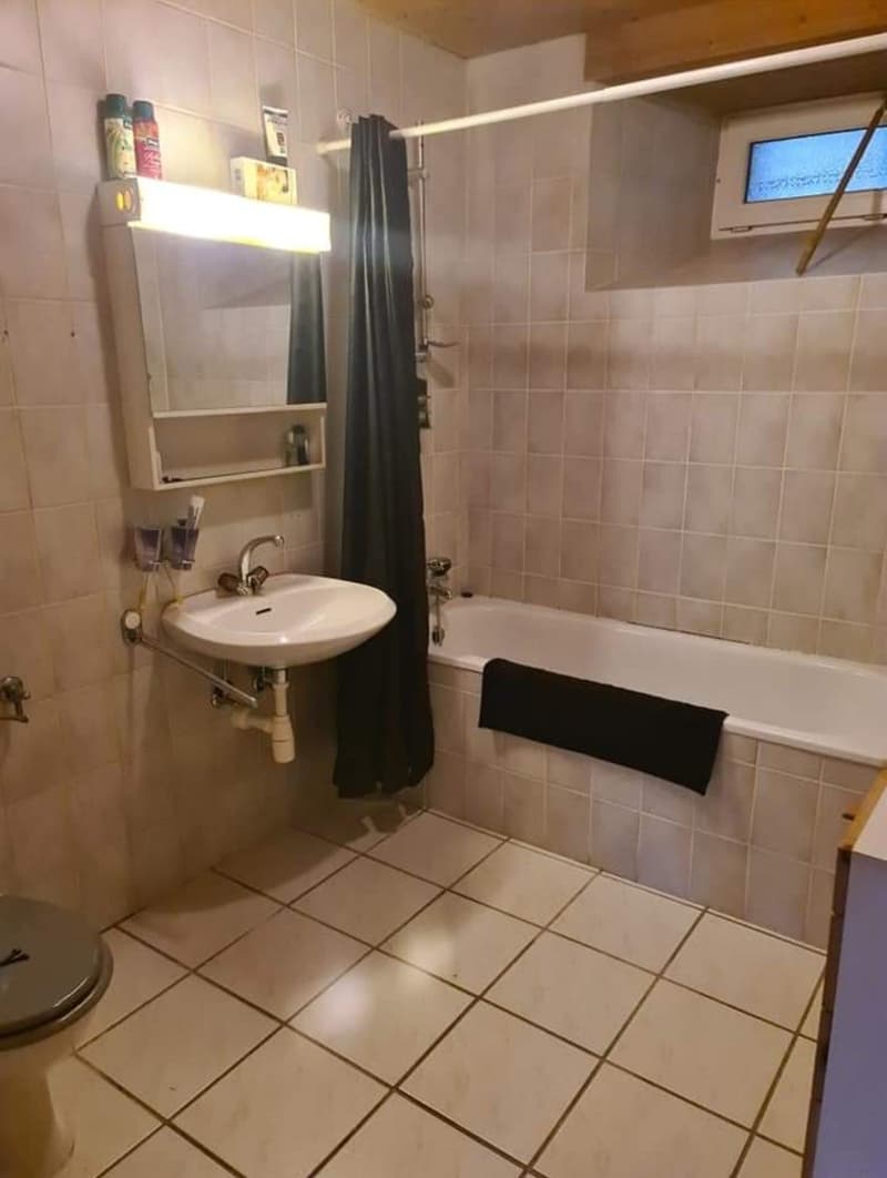 tiled floor, bathtub, sink, shower curtain, mirror with light, toilet, toiletries on shelf, towel on bathtub