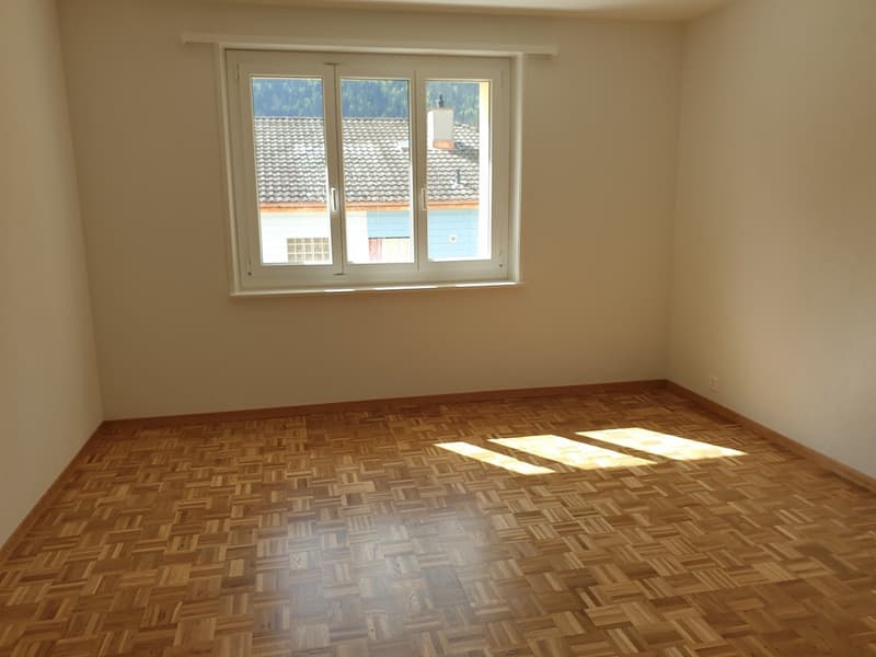 empty room with wooden floor, white walls, large window, sunlight