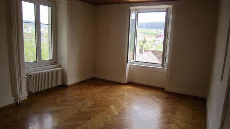empty room, wooden parquet floor, white walls, two large windows, heating radiator, view of the city