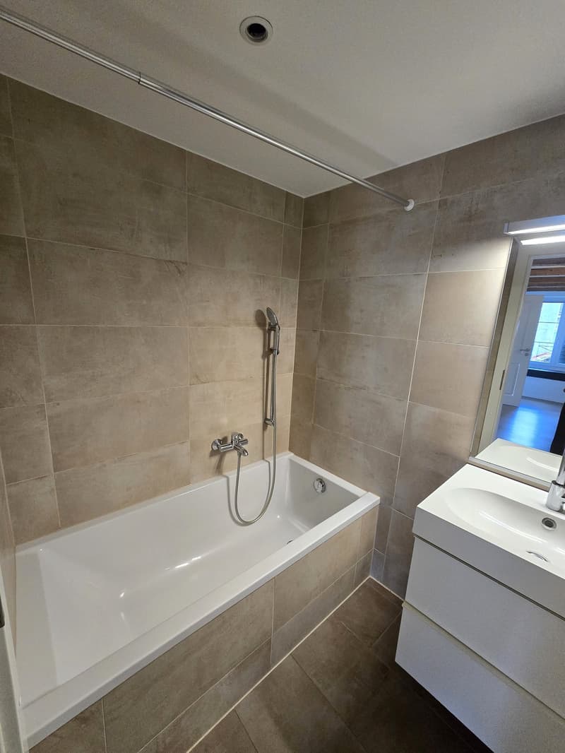 Bathroom with bathtub, sink, mirror, and tiled walls and floor