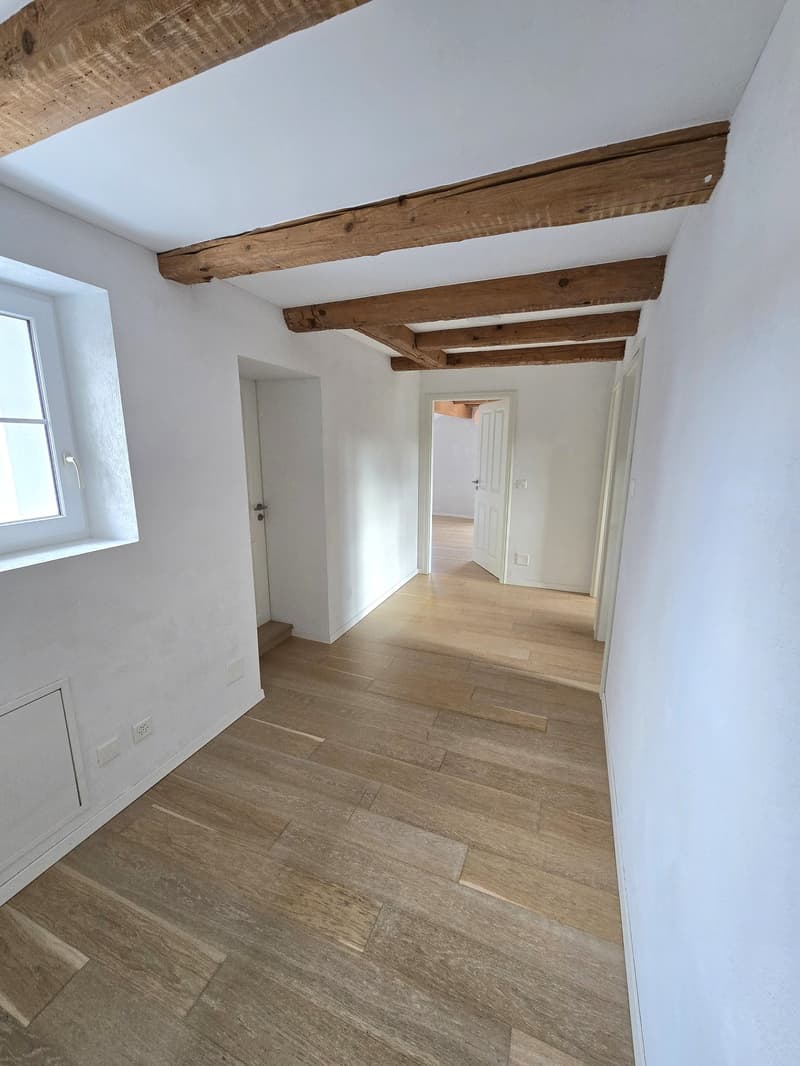 Empty room with wooden floor, white walls, wooden beams, window, doors
