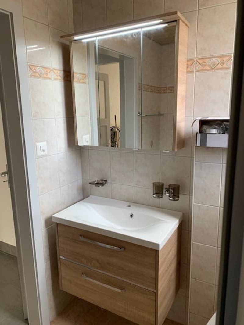 Bathroom with white sink, wooden cabinet, mirror, and tiled walls