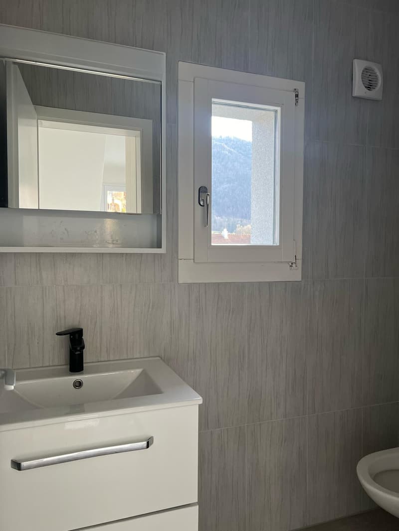 A bathroom with a mirror, white sink, silver faucet, tiled walls, and an exhaust fan.