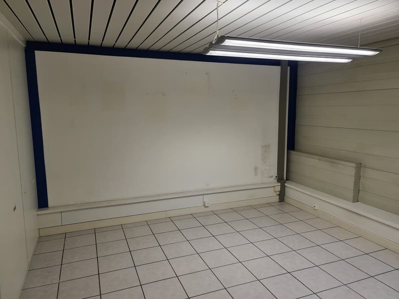 Empty room, white walls, tile floor, two fluorescent ceiling lights, power outlet on the wall, white baseboards.