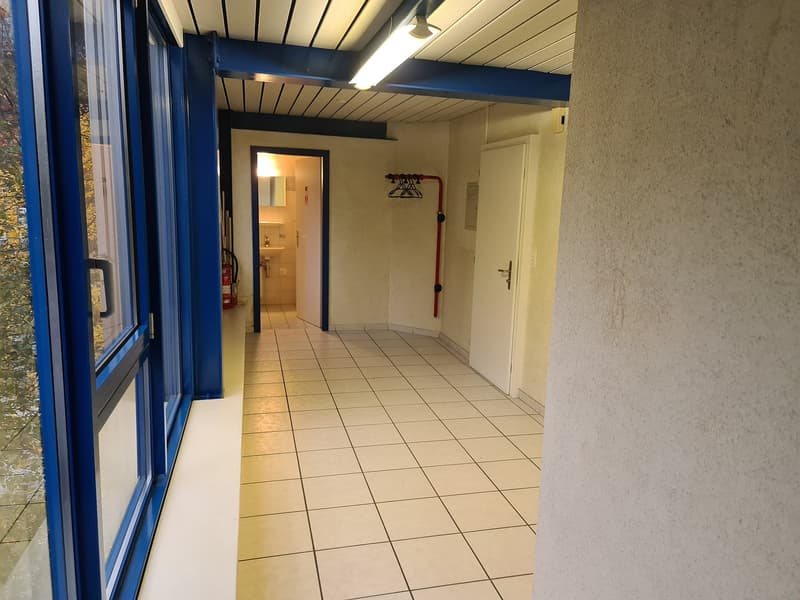 tiled hallway with a ceiling light, white walls, glass doors, fire extinguisher, and a bathroom