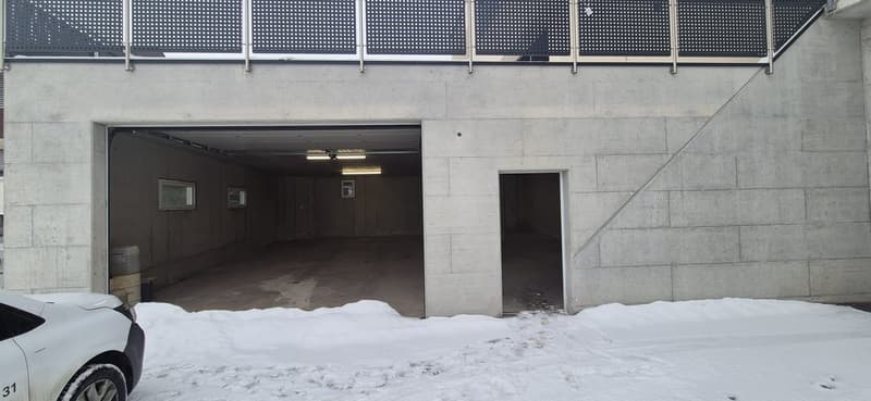 Building exterior with an empty garage, car parked outside in snow, and two rooms on the left side of the garage.