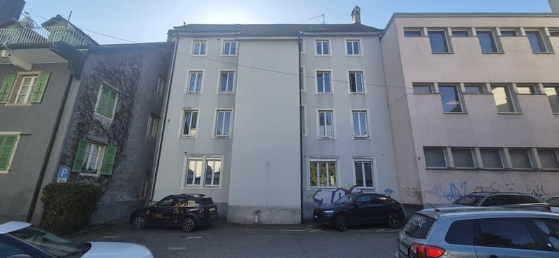 Apartment building with parking in front, multiple stories with windows and balconies