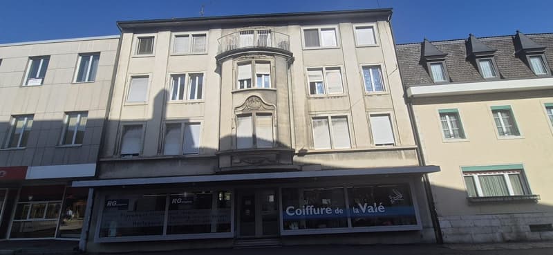 4-story building with balcony, white walls, multiple windows, arched entrance with glass doors, signage
