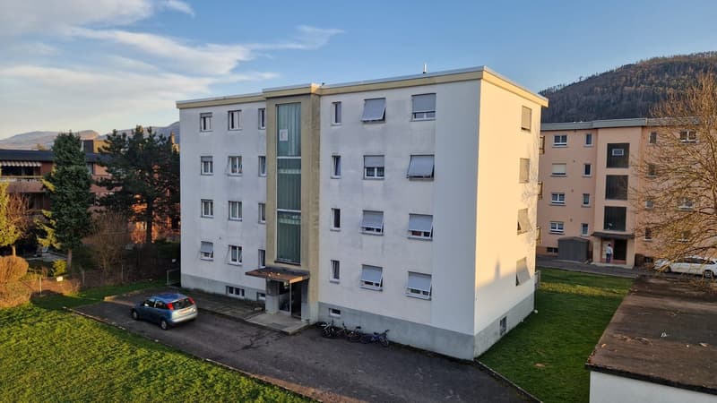 4 story apartment building, white exterior, multiple windows, bicycle parking, car parked at entrance