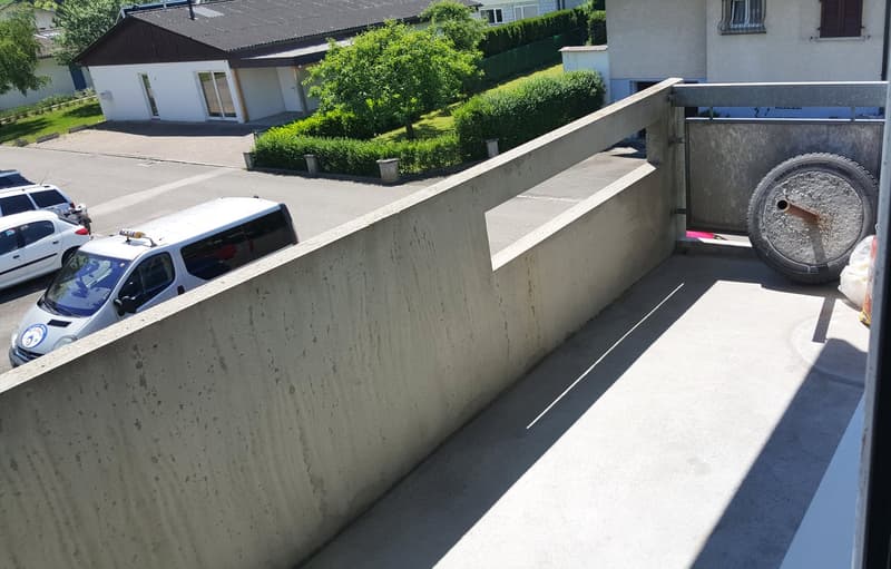 large concrete balcony with a metal railing, view of a parking area with cars