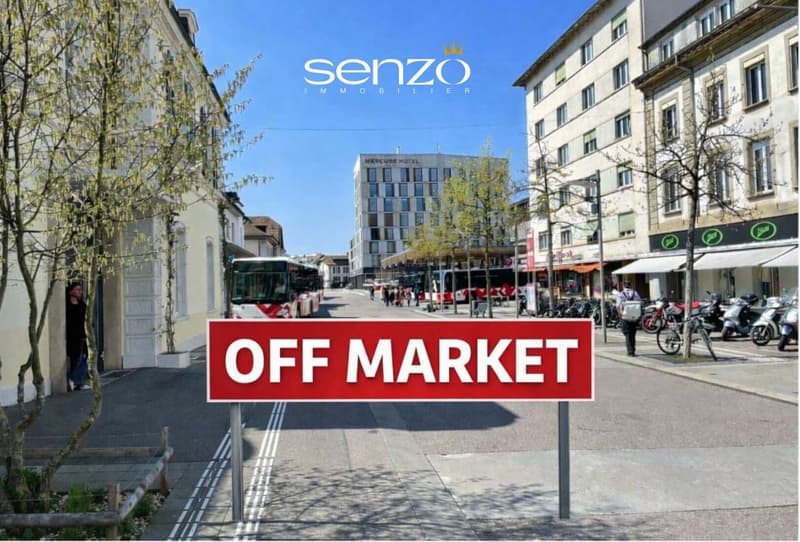 An empty city street with buildings on both sides, buses parked in the street, motorcycles parked in front of stores, an OFF MARKET sign, trees, and a person.