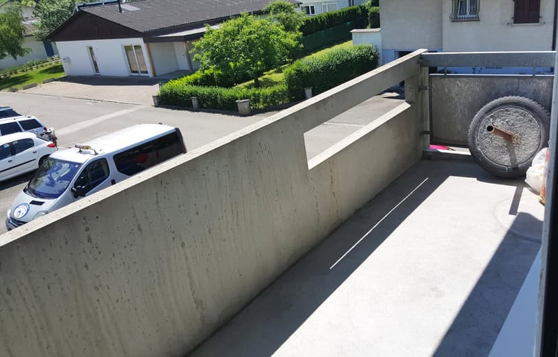 Balcony with concrete floor and wall, overlooking parking lot with cars