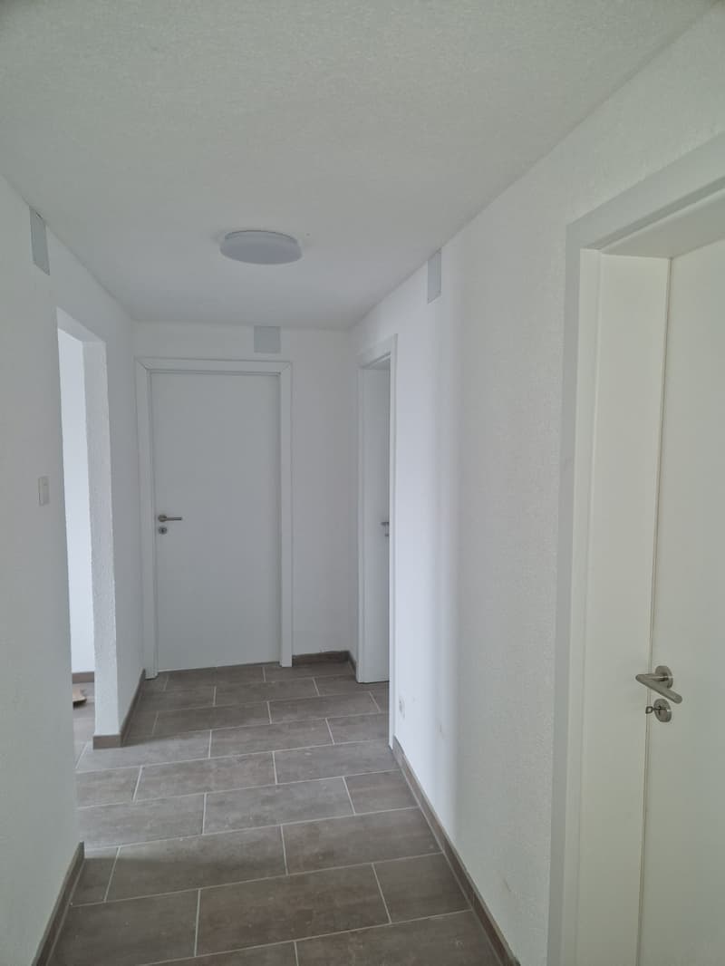Empty hallway with white walls, tiled floor, three doors, ceiling light
