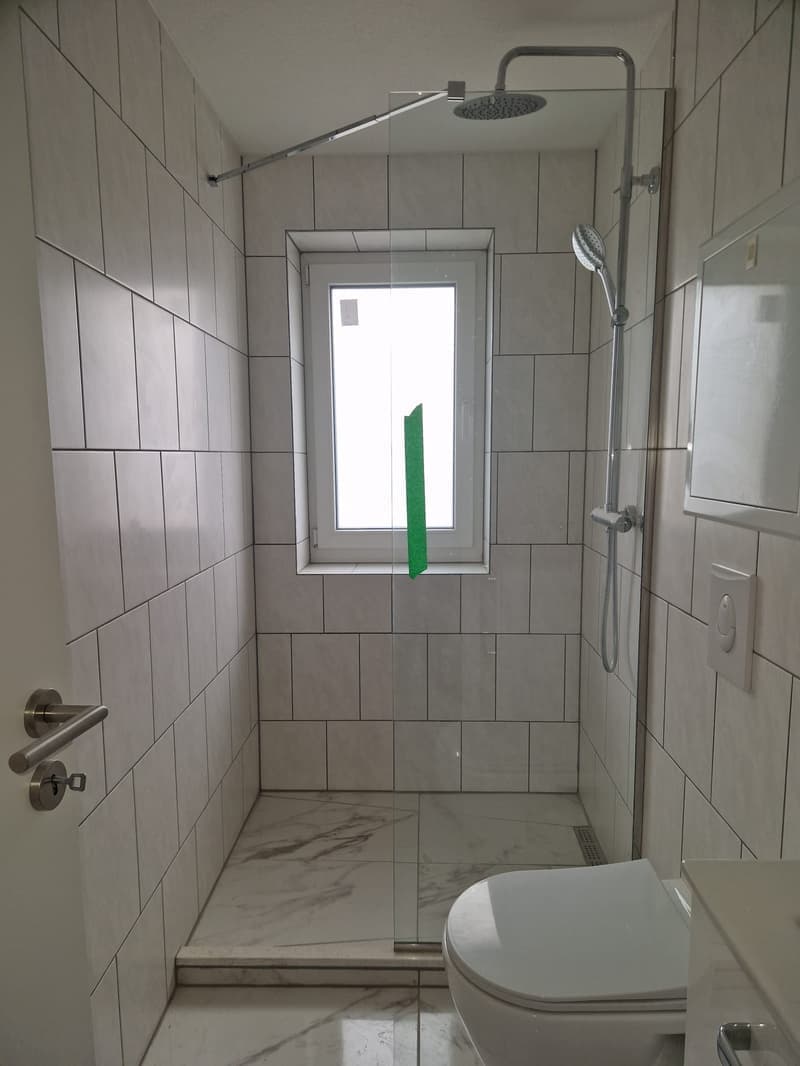 white tiled walls, glass shower enclosure, white toilet, white sink, window