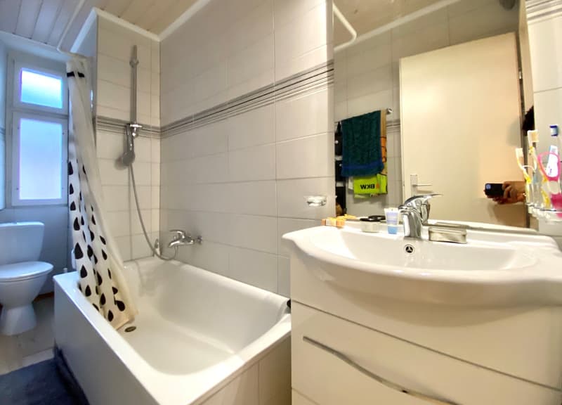 Tiled bathroom with a bathtub, sink, and toilet. There is a towel rack and a private washing machine visible.